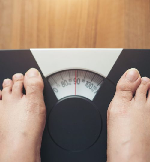 Woman feet standing on Weight Scale on wooden background